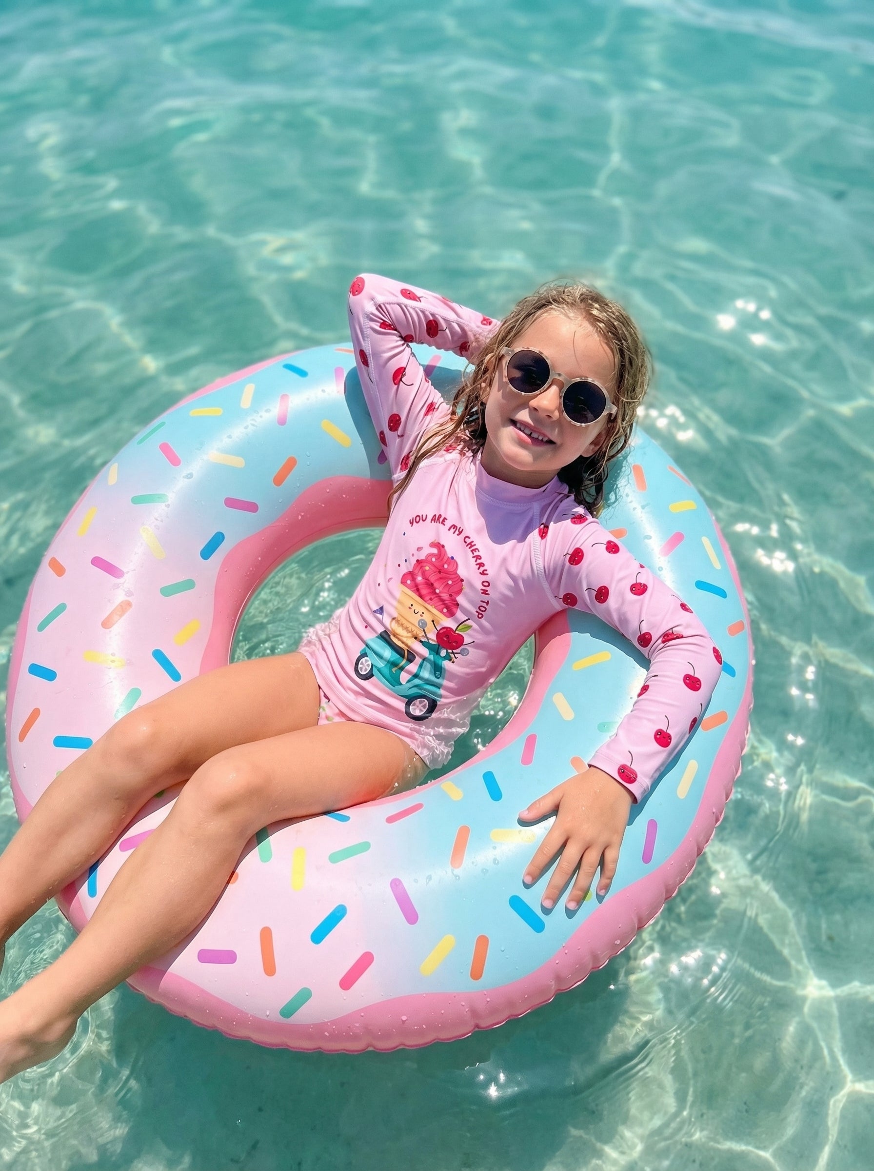 Child in a pink swimsuit with a colorful inflatable ring in clear blue water