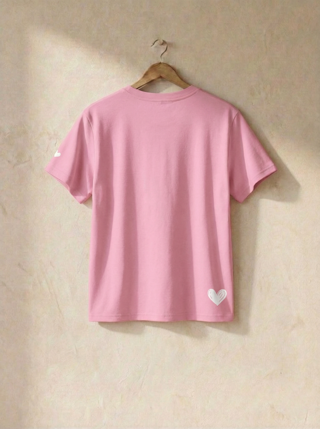Pink t-shirt with a heart design on a hanger against a beige wall