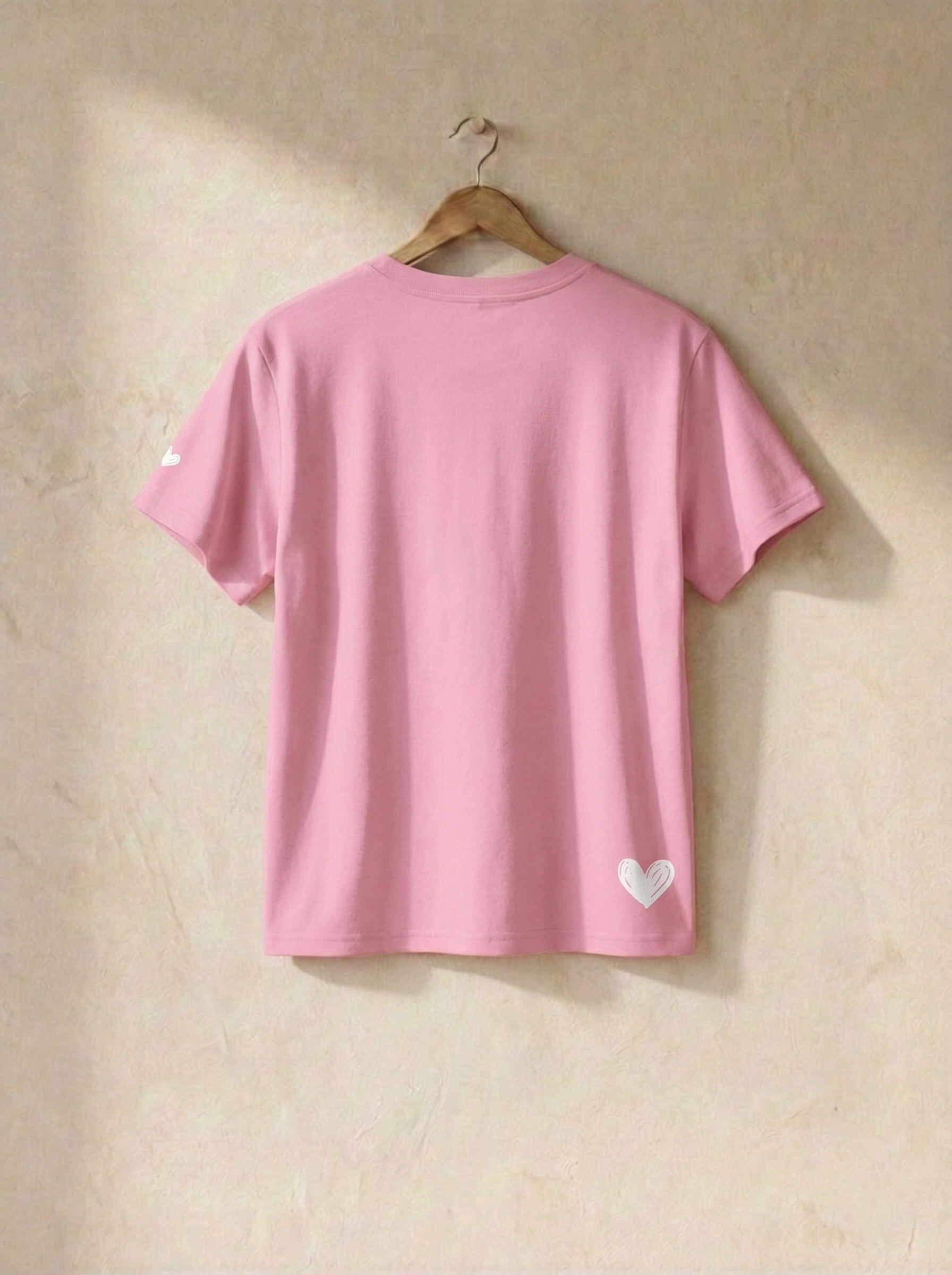 Pink t-shirt with a heart design on a hanger against a beige wall