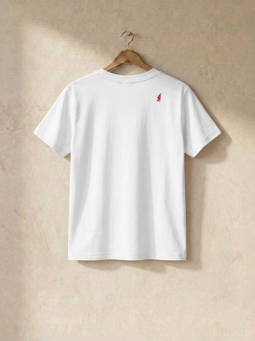 White t-shirt with a small logo on a wooden hanger against a beige wall