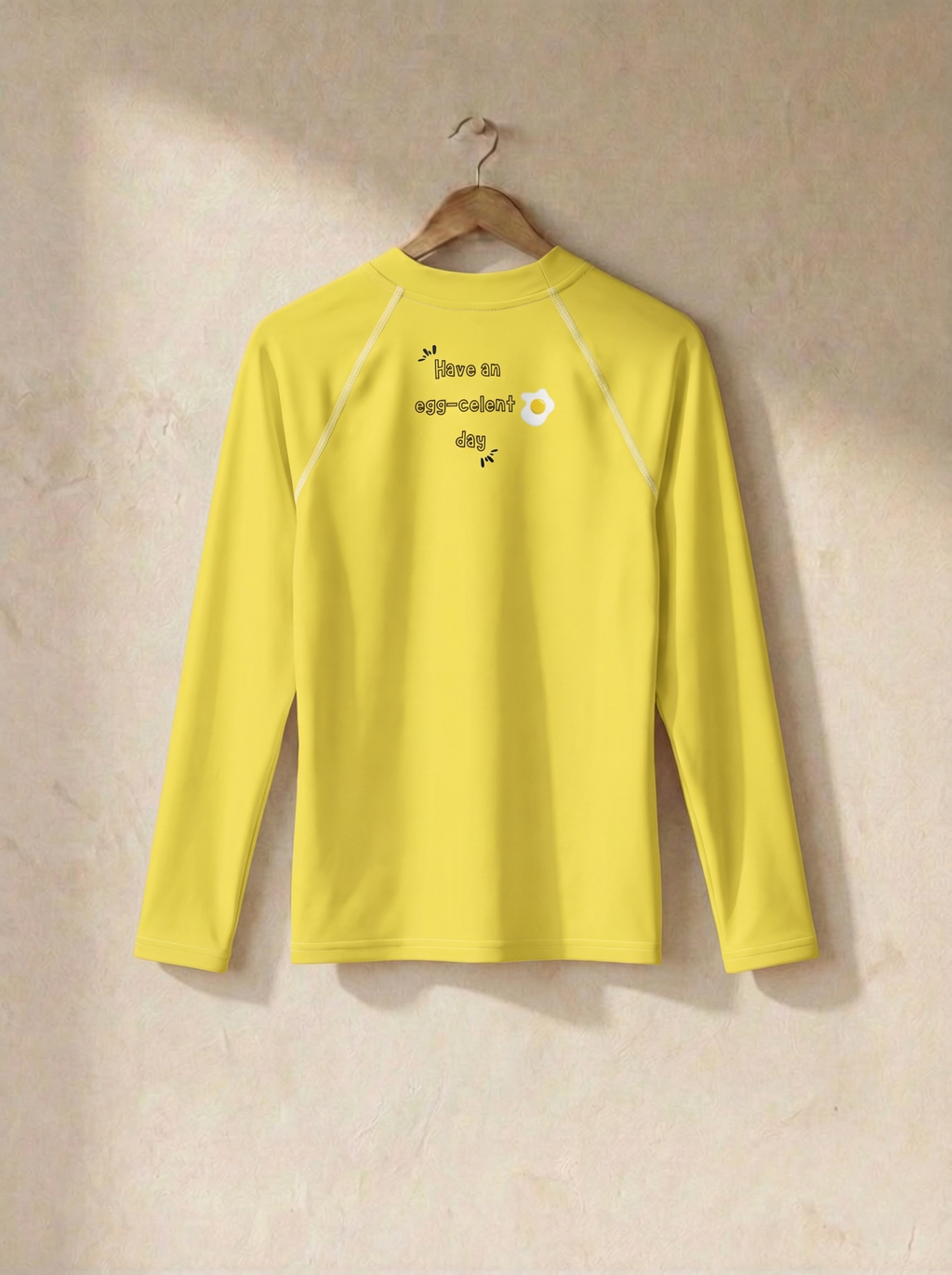 Yellow long-sleeve shirt with text and graphic on a beige background