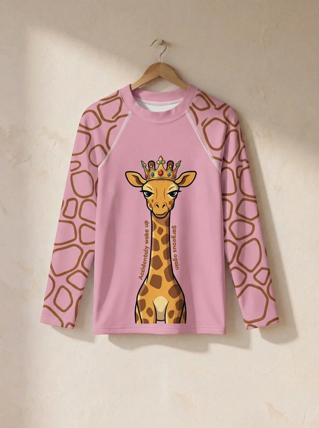 Pink long-sleeve shirt with a giraffe design on a hanger against a beige wall.