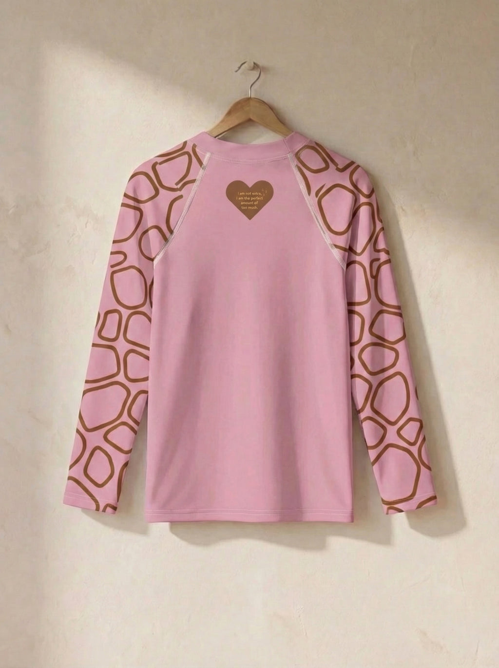 Pink long-sleeve shirt with geometric pattern on sleeves, hanging on a beige wall.