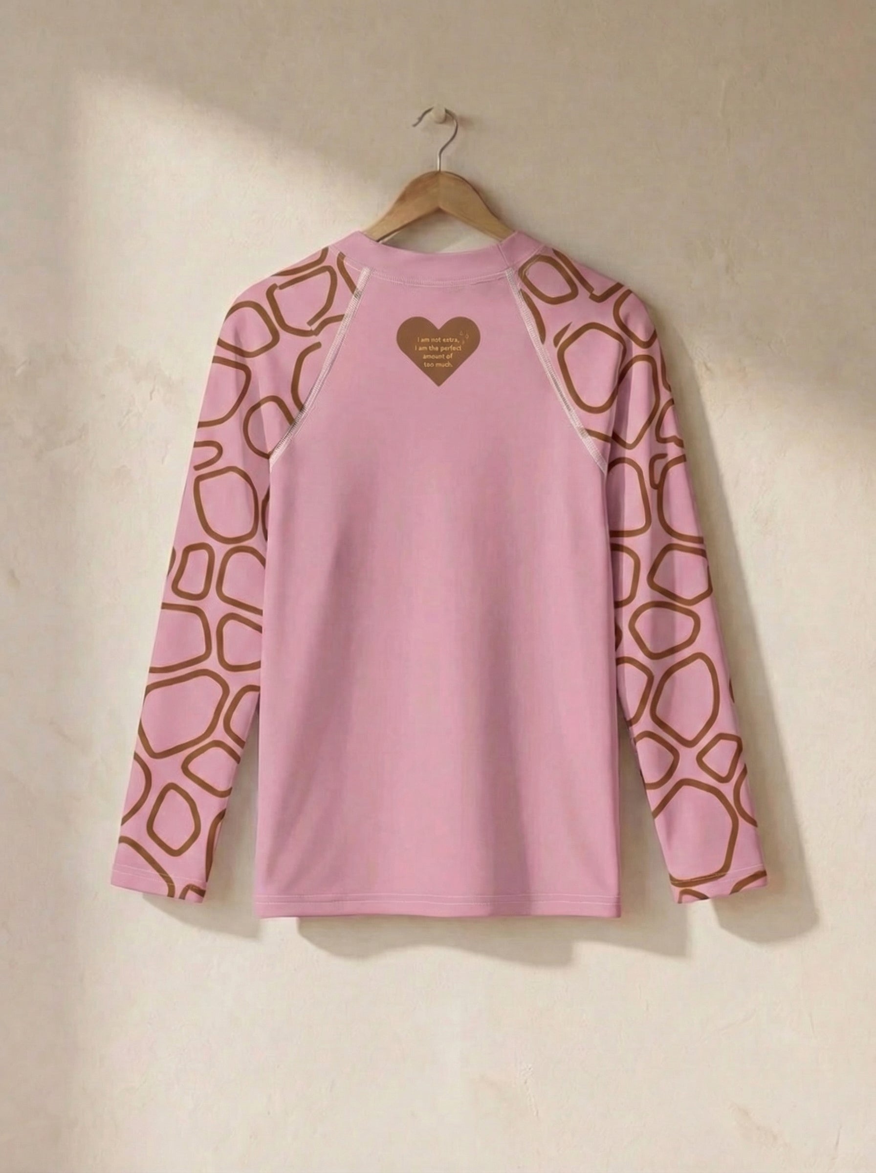 Pink long-sleeve shirt with geometric pattern on sleeves, hanging on a beige wall.