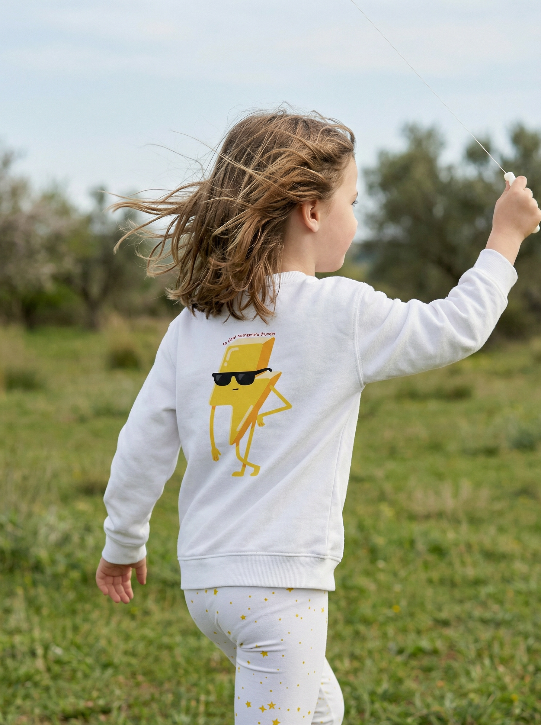 Child wearing a white sweatshirt with a yellow graphic in an outdoor setting